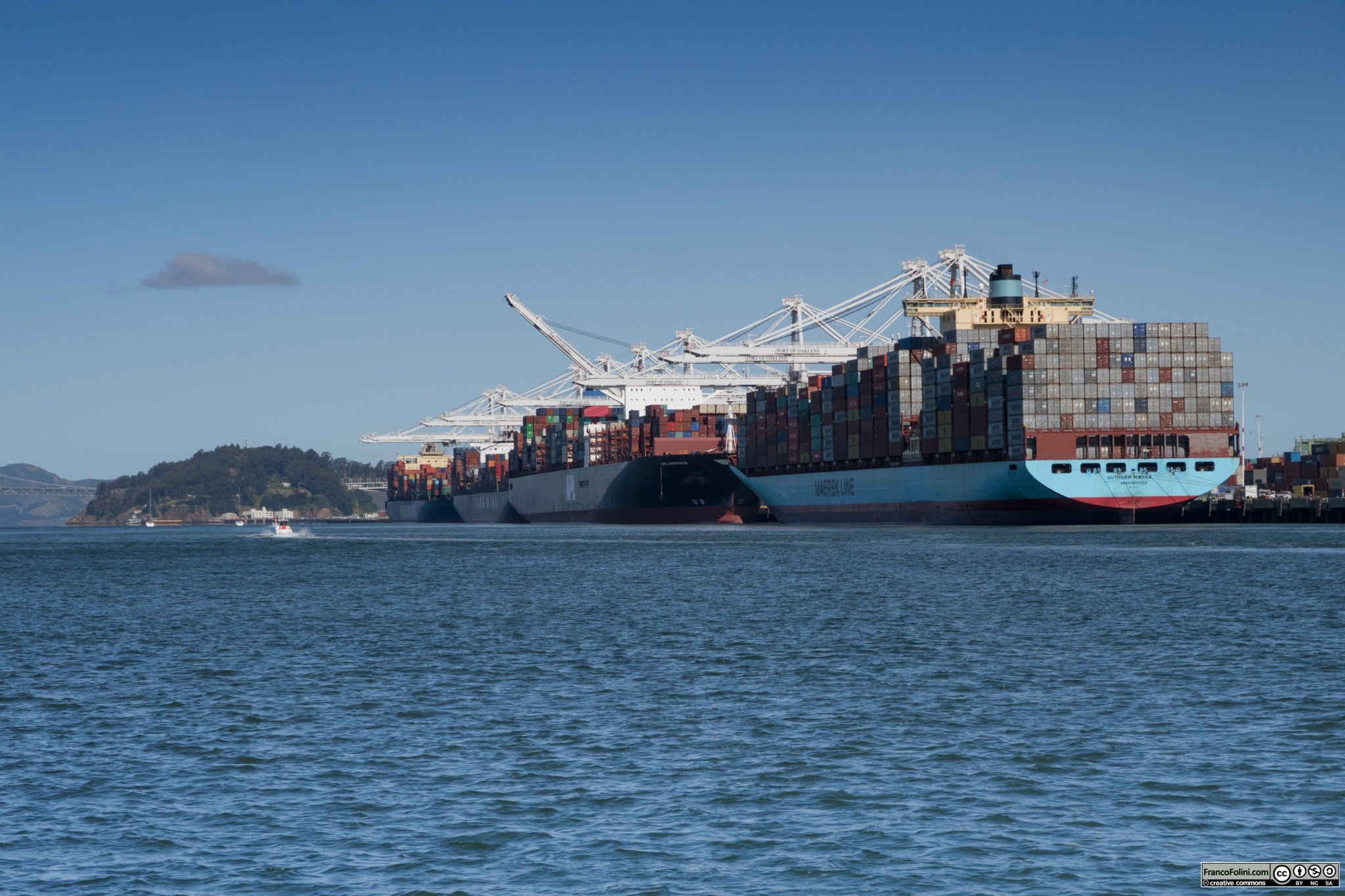 L'affollato porto di Oakland visto dall'isola di Alameda. Si notano le immancabili navi porta-container che vengono caricate e scaricate dalle immense gru bianche visibili sullo sfondo. Il porto di Oakland è il quinto porto più importante degli Stati Uniti